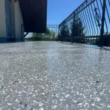 Balkon z nowoczesną podłogą na balkonie z powłok wodoszczelnych. Błyszcząca powierzchnia z szarymi i białymi płatkami, metalowa balustrada i błękitne niebo.