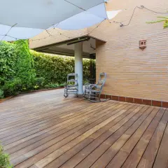 Drewniany taras z bujną zielenią i dwoma fotelami bujanymi. Tani taras inspiracje na relaks w ogrodzie.