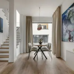 Nowoczesny salon z jadalnią, gdzie drewniany flok na podłodze tworzy ciepłą bazę dla białych ścian i minimalistycznych mebli.