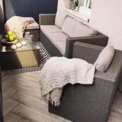 Przytulny balkon w bloku z wielkiej płyty, z meblami rattanowymi, kocami i stolikiem kawowym.