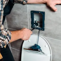 Mężczyzna w kratę naprawia mechanizm spłuczki toaletowej.