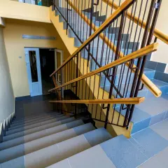 Schody wyłożone szarą terakotą, z żółtymi ścianami i metalową balustradą z drewnianymi poręczami.