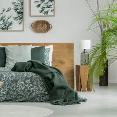 Sypialnia w stylu boho z drewnianym łóżkiem i pościelą w liście. Kolor khaki z czym łączyć? Z zielenią roślin i naturalnymi materiałami.