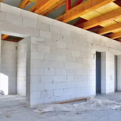 Wnętrze domu w budowie, ściany z bloczków suporeks, widoczne drewniane belki stropowe.