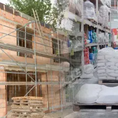 Budowa domu w toku, obok magazyn materiałów budowlanych. Wpływ cen materiałów budowlanych na inwestycje.