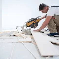 Budowlaniec przycina panele winylowe piłą ukośnicą.