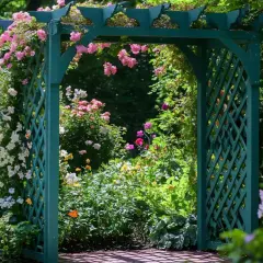 Zielona pergola DIY, ozdobiona kwitnącymi różami i innymi kwiatami, tworzy malownicze przejście do ogrodu pełnego zieleni.