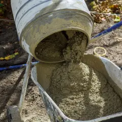 Mieszanka betonu wylewa się z betoniarki do taczki. Prawidłowe proporcje betonu są kluczowe dla jego wytrzymałości.