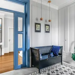 Elegancki przedpokój z czarną ławką i zieloną torbą. Ściana pomalowana na jasny kolor, idealna jako baza do wyboru dekoracji, co na ścianę w przedpokoju żeby się nie brudziła.