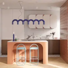 Nowoczesna kuchnia z pomarańczową wyspą i dwoma turkusowymi hokerami. Nad wyspą wisi designerska lampa.