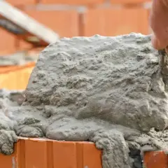 Ręka murarza nakłada świeżą zaprawę na cegły.