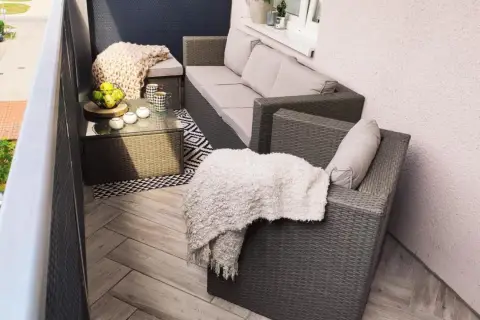Przytulny balkon w bloku z wielkiej płyty, z meblami rattanowymi, kocami i stolikiem kawowym.