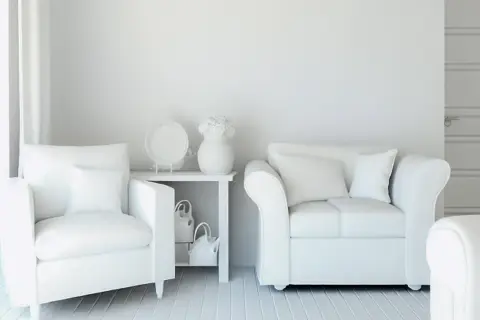 Białe fotele i sofa w odcieniu ral 9010, stolik z wazonem i dekoracjami, tworzą minimalistyczną przestrzeń.