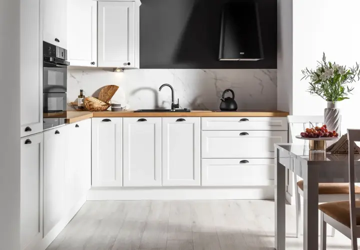 Biała kuchnia na wymiar z drewnianym blatem, czarnym okapem i marmurowym backsplash. Zastanawiasz się, ile kosztuje kuchnia na wymiar?