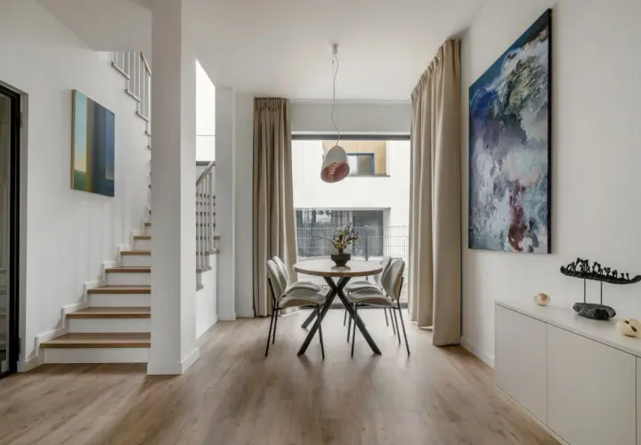 Nowoczesny salon z jadalnią, gdzie drewniany flok na podłodze tworzy ciepłą bazę dla białych ścian i minimalistycznych mebli.