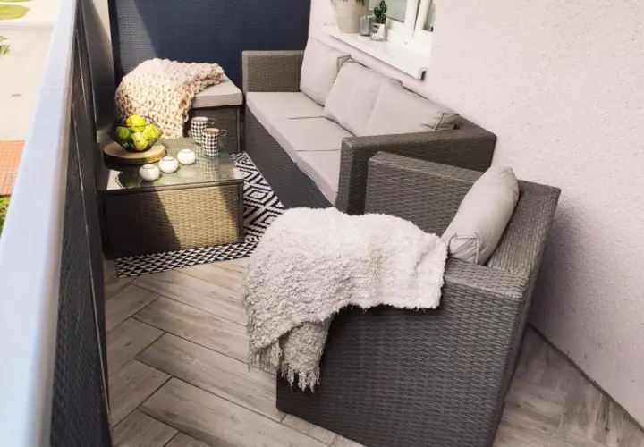 Przytulny balkon w bloku z wielkiej płyty, z meblami rattanowymi, kocami i stolikiem kawowym.