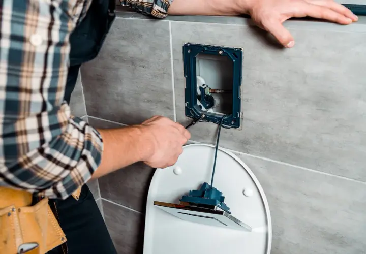 Mężczyzna w kratę naprawia mechanizm spłuczki toaletowej.