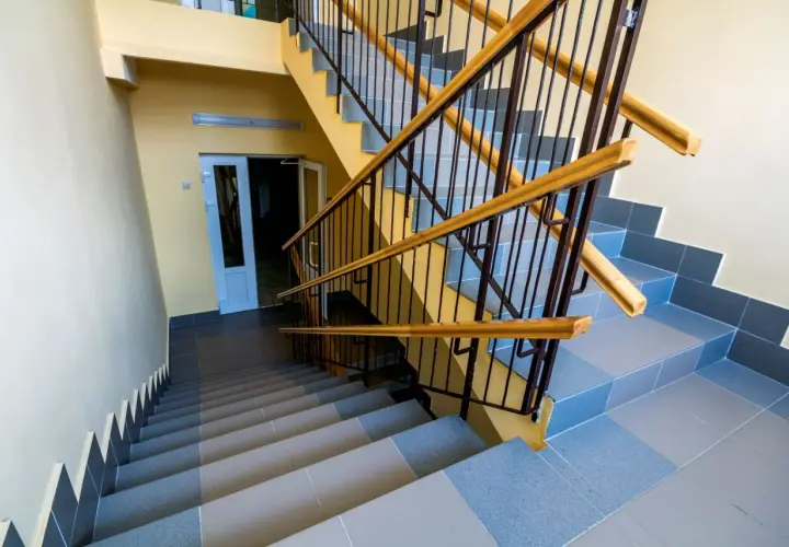 Schody wyłożone szarą terakotą, z żółtymi ścianami i metalową balustradą z drewnianymi poręczami.