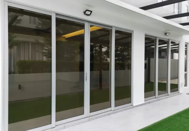 Nowoczesne drzwi tarasowe ze szkłem dymionym, odbijające zieleń ogrodu i architekturę domu.