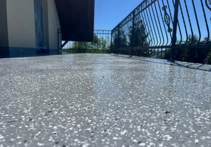 Balkon z nowoczesną podłogą na balkonie z powłok wodoszczelnych. Błyszcząca powierzchnia z szarymi i białymi płatkami, metalowa balustrada i błękitne niebo.