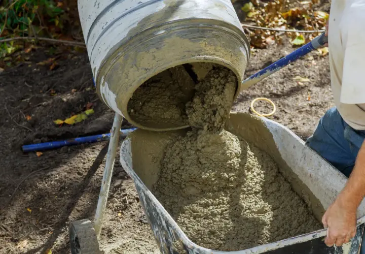 Mieszanka betonu wylewa się z betoniarki do taczki. Prawidłowe proporcje betonu są kluczowe dla jego wytrzymałości.