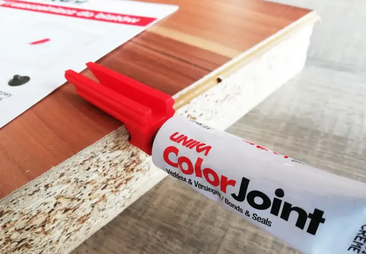 Klej do blatów ColorJoint i czerwony aplikator na krawędzi płyty meblowej.