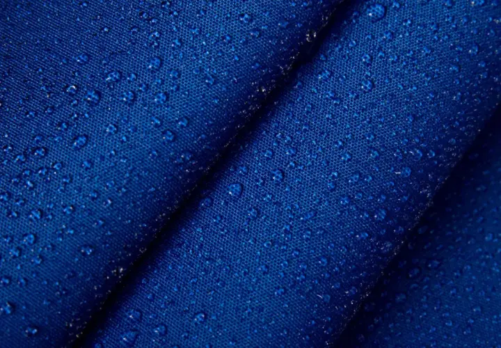 Krople wody na granatowym, **hydrofobowym** materiale. Tekstura tkaniny jest wyraźnie widoczna pod kropelkami.