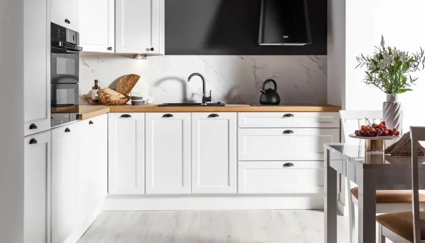 Biała kuchnia na wymiar z drewnianym blatem, czarnym okapem i marmurowym backsplash. Zastanawiasz się, ile kosztuje kuchnia na wymiar?