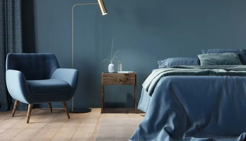 Przytulna sypialnia w odcieniach **kolor navy**. Miękki fotel, łóżko z pościelą i zasłony tworzą spokojną atmosferę.