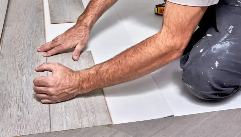 Układanie paneli winylowych na płytkach. Ręce montażysty dopasowują deski.