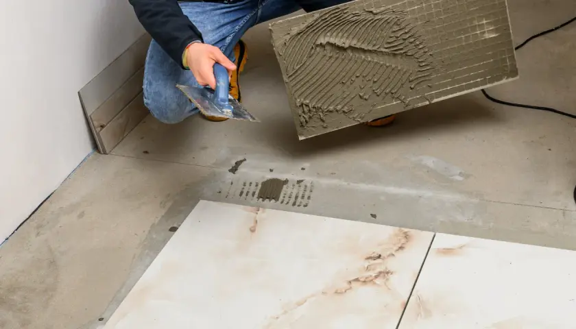 Układanie płytek 120x20 cena. Ręczne nakładanie kleju na dużą płytkę przed położeniem jej na podłodze.