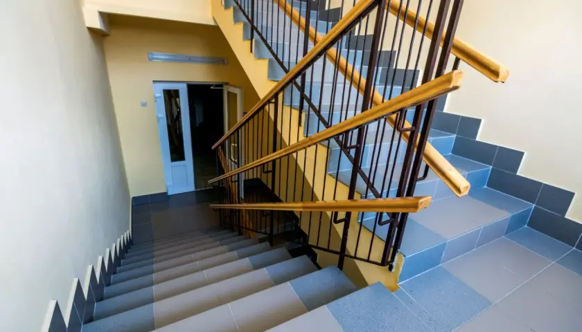 Schody wyłożone szarą terakotą, z żółtymi ścianami i metalową balustradą z drewnianymi poręczami.