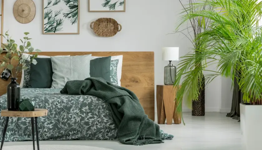 Sypialnia w stylu boho z drewnianym łóżkiem i pościelą w liście. Kolor khaki z czym łączyć? Z zielenią roślin i naturalnymi materiałami.