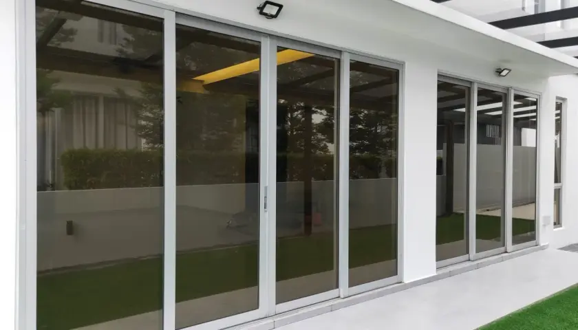 Nowoczesne drzwi tarasowe ze szkłem dymionym, odbijające zieleń ogrodu i architekturę domu.