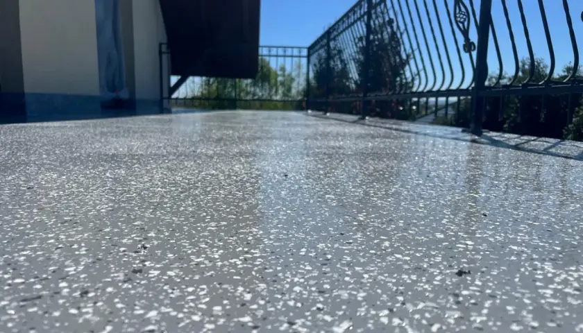 Balkon z nowoczesną podłogą na balkonie z powłok wodoszczelnych. Błyszcząca powierzchnia z szarymi i białymi płatkami, metalowa balustrada i błękitne niebo.
