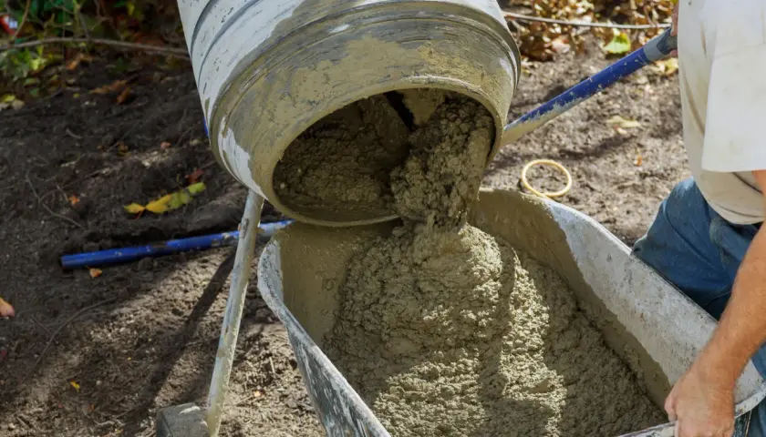 Mieszanka betonu wylewa się z betoniarki do taczki. Prawidłowe proporcje betonu są kluczowe dla jego wytrzymałości.