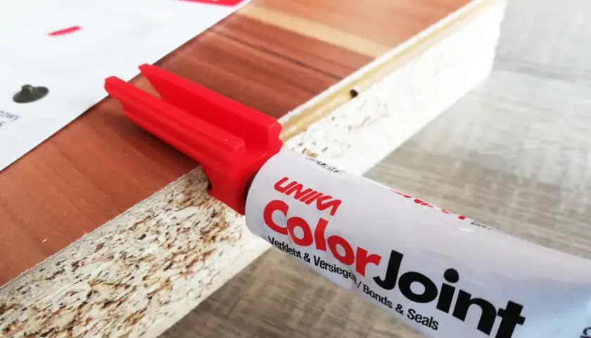 Klej do blatów ColorJoint i czerwony aplikator na krawędzi płyty meblowej.