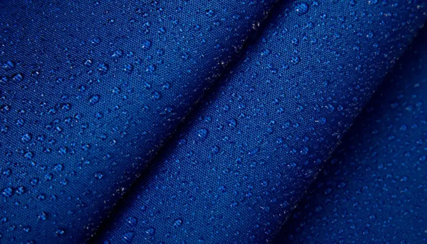 Krople wody na granatowym, **hydrofobowym** materiale. Tekstura tkaniny jest wyraźnie widoczna pod kropelkami.