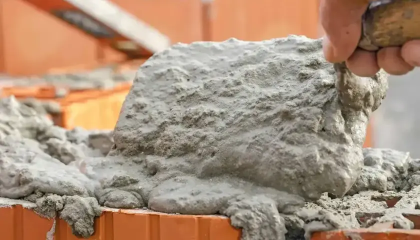 Ręka murarza nakłada świeżą zaprawę na cegły.