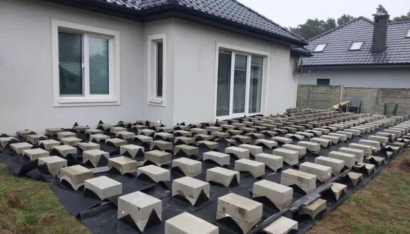 Budowa tarasu drewnianego na bloczkach betonowych. Podkład z agrowłókniny i betonowe podpory czekają na deski.