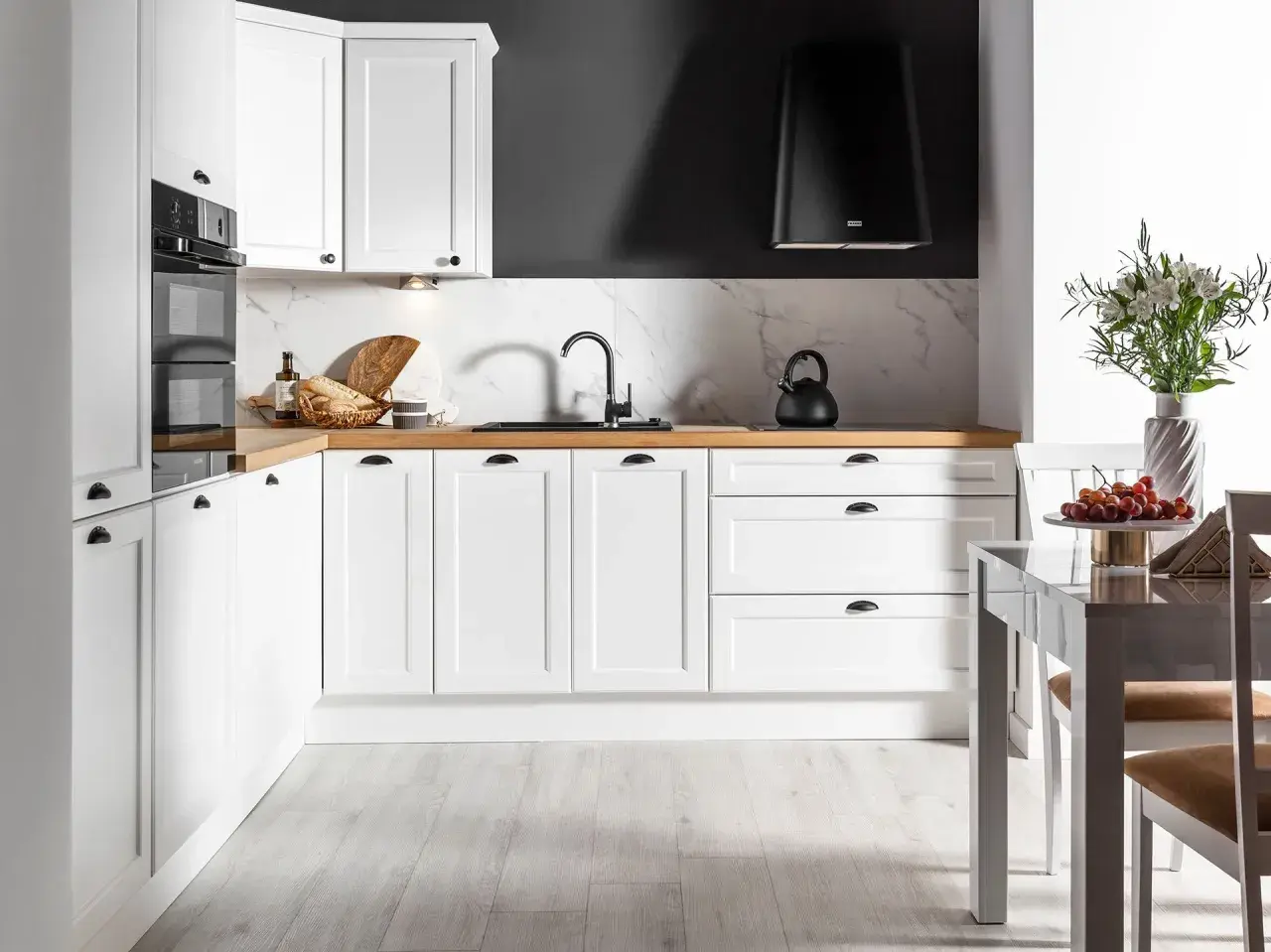 Biała kuchnia na wymiar z drewnianym blatem, czarnym okapem i marmurowym backsplash. Zastanawiasz się, ile kosztuje kuchnia na wymiar?