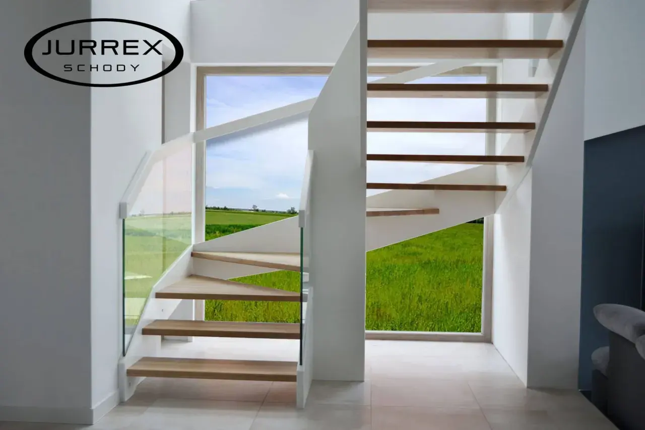 Nowoczesne schody policzkowe z drewnianymi stopniami i szklaną balustradą, z widokiem na zielone pole.