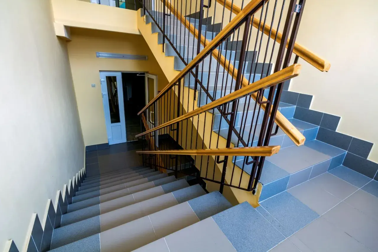 Schody wyłożone szarą terakotą, z żółtymi ścianami i metalową balustradą z drewnianymi poręczami.