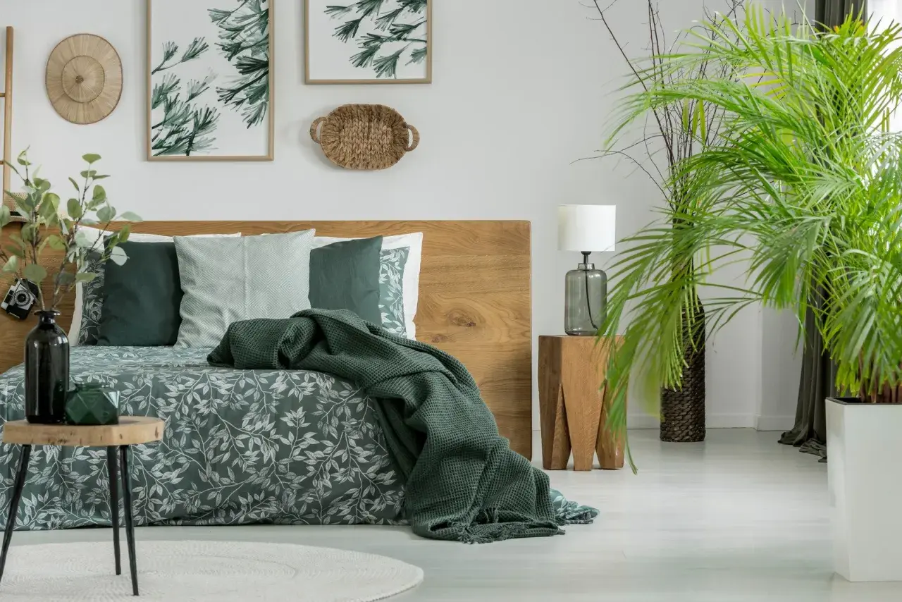Sypialnia w stylu boho z drewnianym łóżkiem i pościelą w liście. Kolor khaki z czym łączyć? Z zielenią roślin i naturalnymi materiałami.