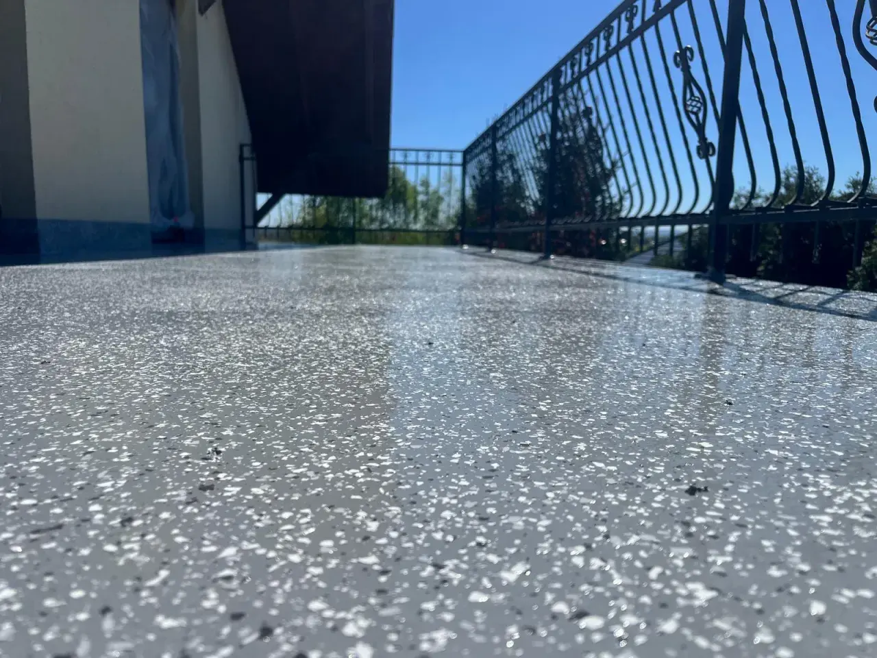 Balkon z nowoczesną podłogą na balkonie z powłok wodoszczelnych. Błyszcząca powierzchnia z szarymi i białymi płatkami, metalowa balustrada i błękitne niebo.