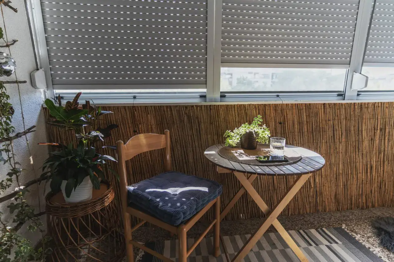 Przytulny balkon wnękowy z drewnianym krzesłem, stolikiem i roślinami. Idealne miejsce na poranną kawę.