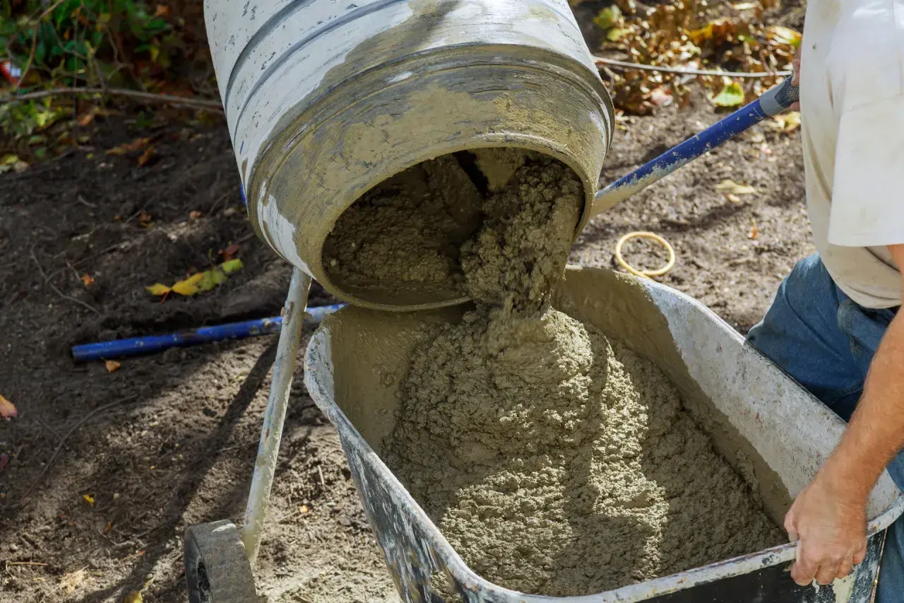Mieszanka betonu wylewa się z betoniarki do taczki. Prawidłowe proporcje betonu są kluczowe dla jego wytrzymałości.