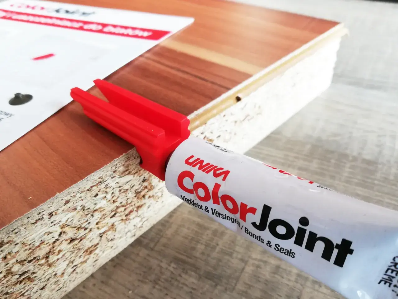 Klej do blatów ColorJoint i czerwony aplikator na krawędzi płyty meblowej.