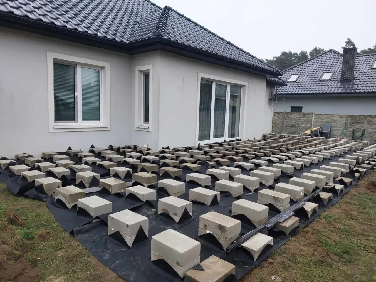 Budowa tarasu drewnianego na bloczkach betonowych. Podkład z agrowłókniny i betonowe podpory czekają na deski.