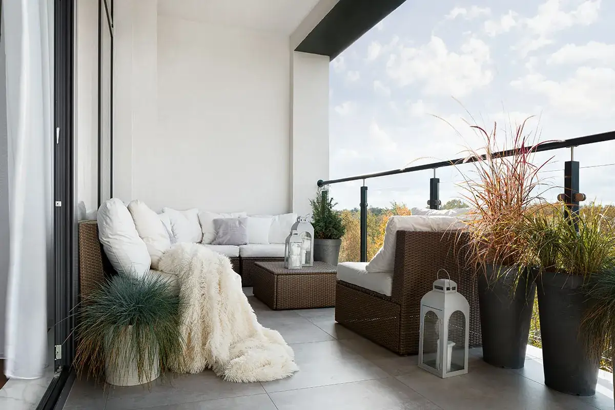 Przytulna loggia z wygodnym rattanowym narożnikiem, puszystym kocem i ozdobnymi latarniami. Balkon zaprasza do relaksu wśród zieleni.